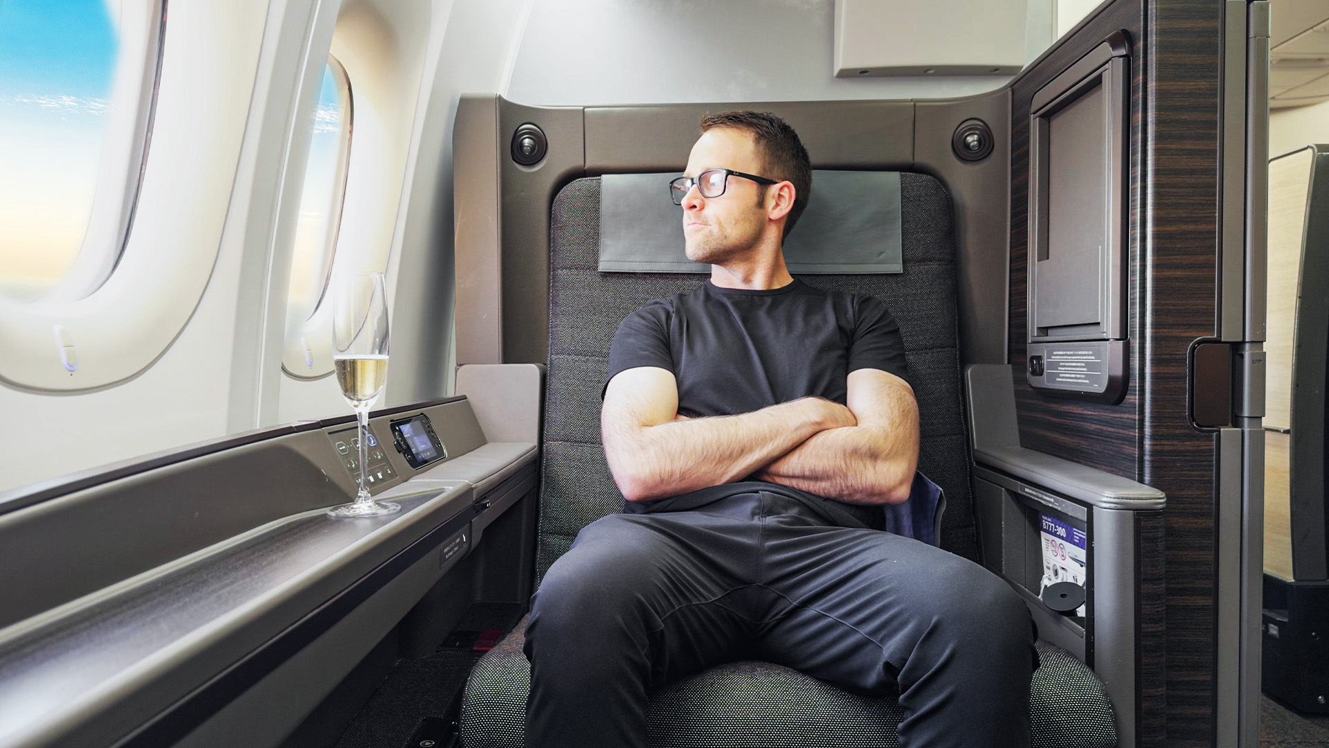 Nik sitting in First class looking out the window drinking Champagne