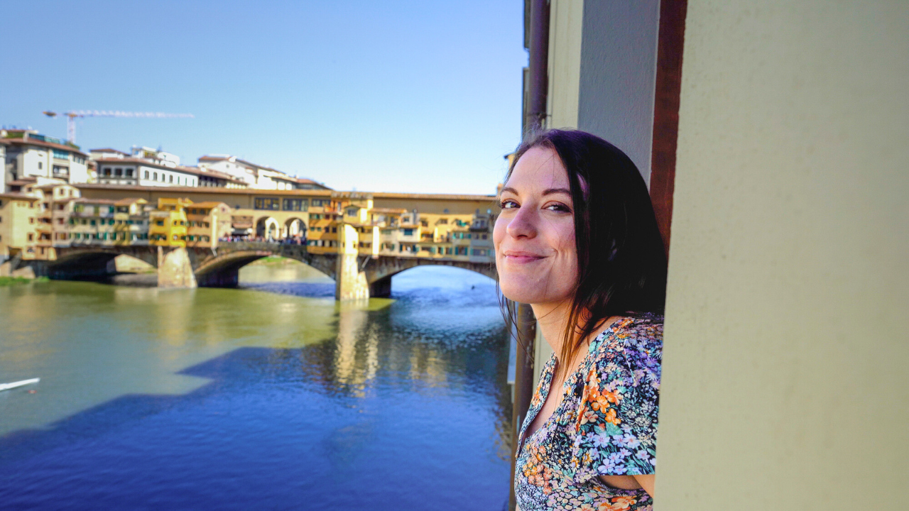 Allie leaning out a window in front of a beautiful bridge in europe